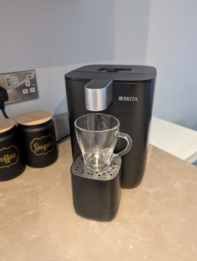 Clear glass cup on the drip tray directly under the spout of a black BRITA water dispenser