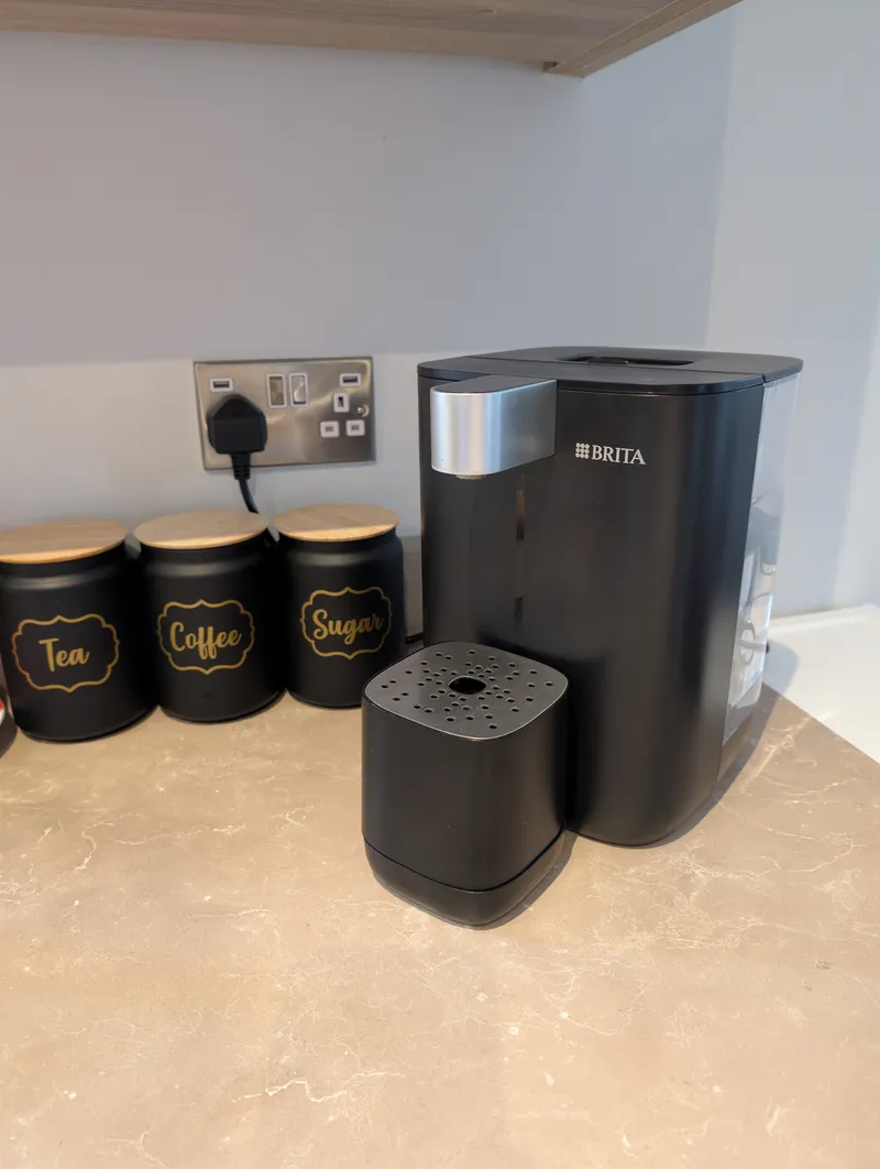 Side view of a black BRITA water dispenser showing the clear water tank at the side and the square drip tray at the front